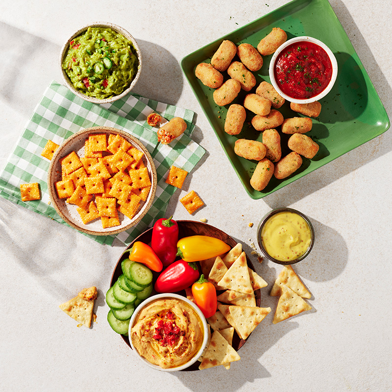 Pizza bites on a table with Cheez-It crackers and dipping vegetables. 