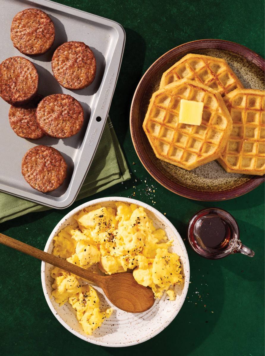 Sausage patties on a plate with waffles and scrambled eggs.