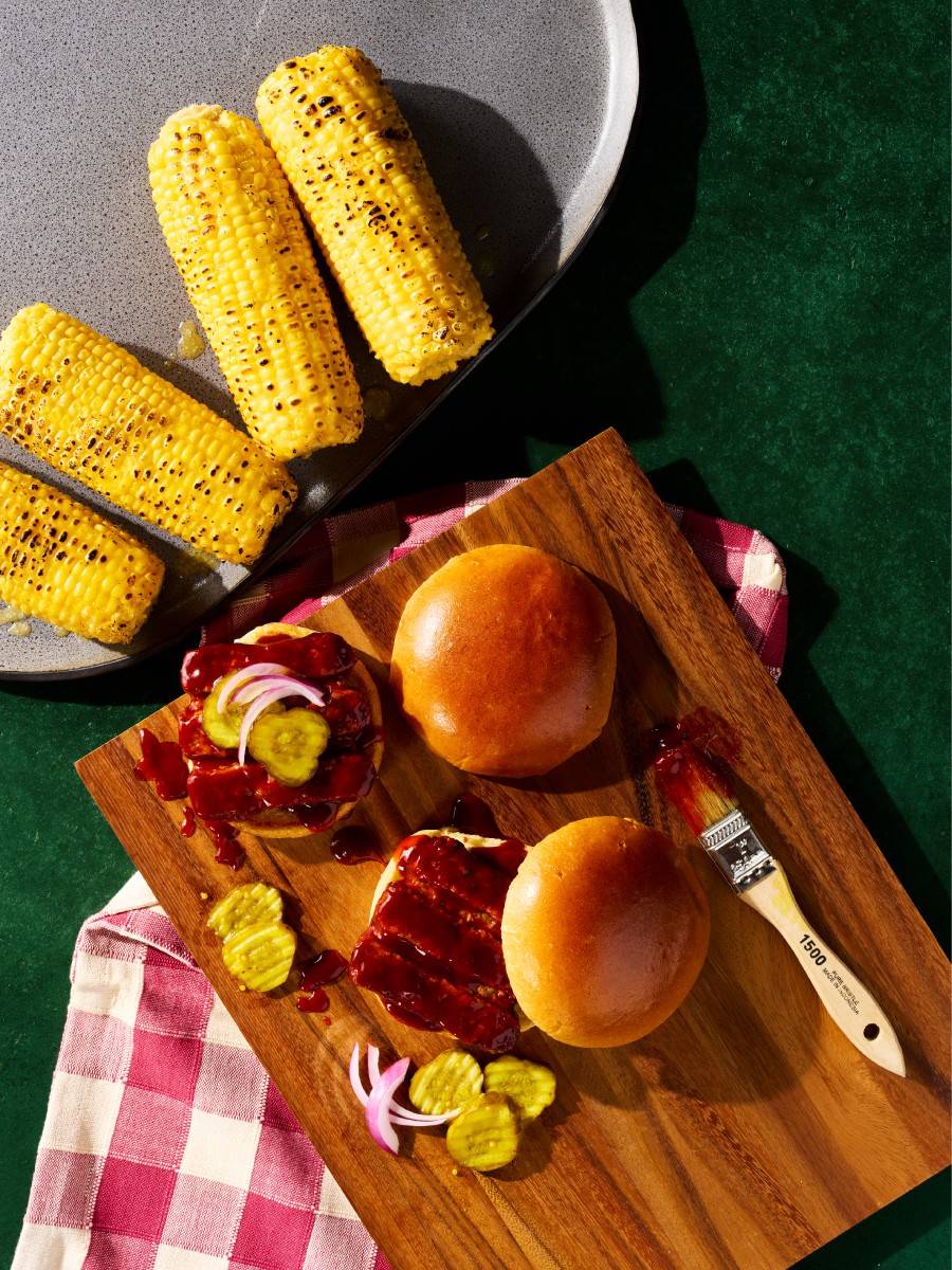 Riblets on a hamburger bun with corn on the cob.