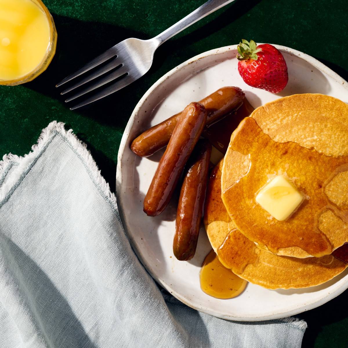 Sausage links on a plate with pancakes and a strawberry.